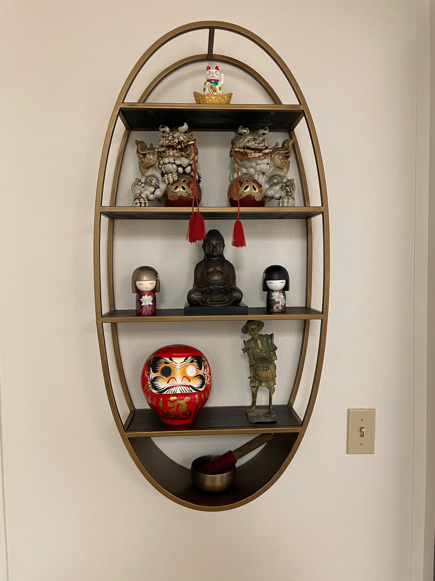 A stylish set of oval shelves with a Buddha on it.
